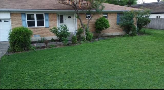 ranch-style home featuring a front lawn, fence, a garage, and brick siding