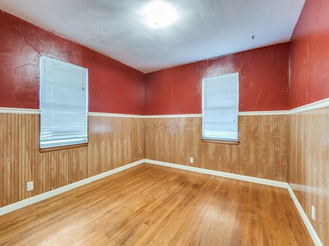 1413 Sylvan Dr, Arlington, TX 76012 - empty room featuring a wainscoted wall, wood walls, wood finished floors, and a wealth of natural light