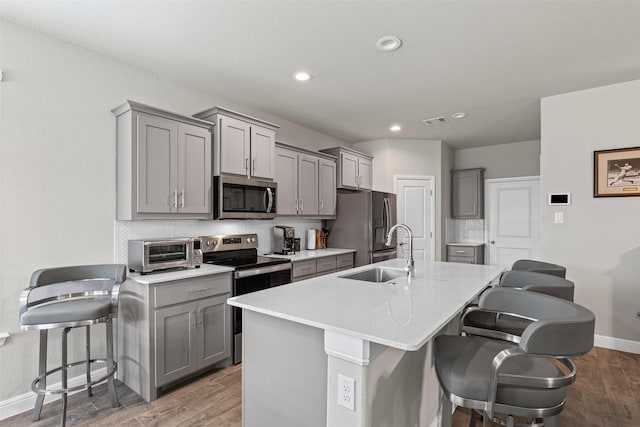 kitchen with a breakfast bar area, a sink, stainless steel appliances, a toaster, and gray cabinets