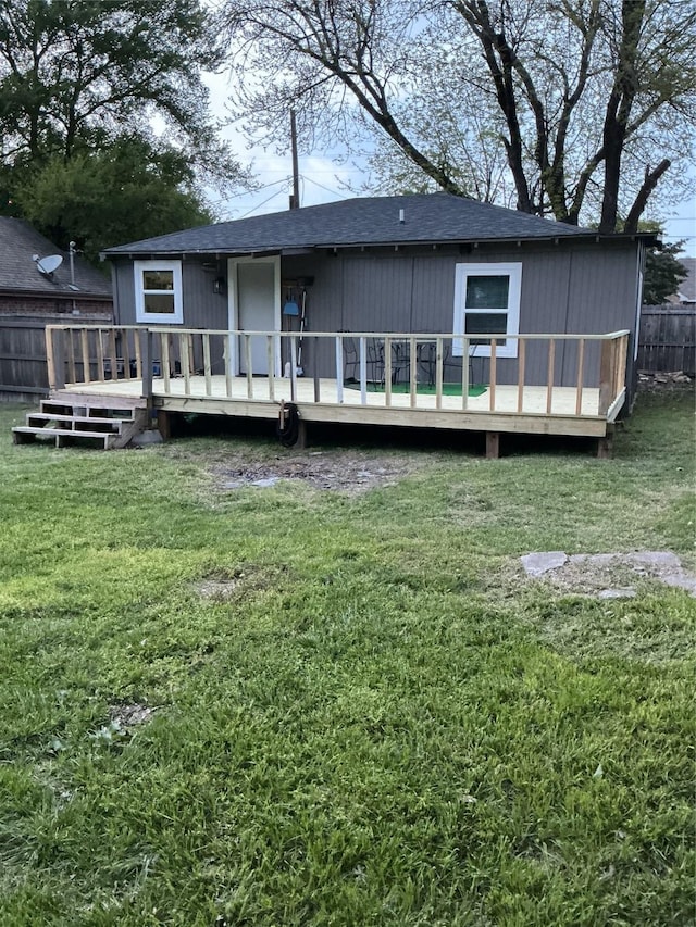 rear view of house featuring fence, roof with shingles, a deck, and a yard