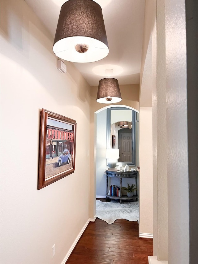 hall featuring baseboards, arched walkways, and dark wood-style floors