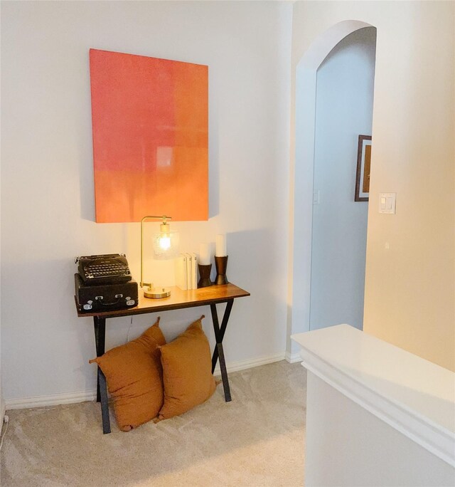 hallway with arched walkways, baseboards, and light carpet