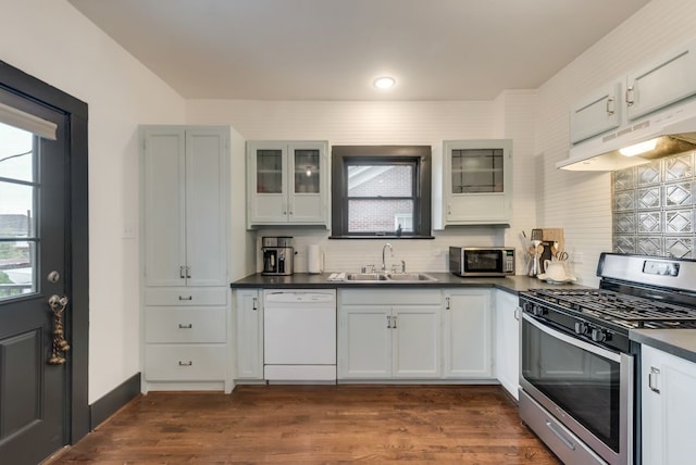 kitchen featuring glass insert cabinets, under cabinet range hood, appliances with stainless steel finishes, dark countertops, and a sink