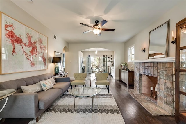 living area featuring visible vents, arched walkways, dark wood finished floors, a tiled fireplace, and a ceiling fan