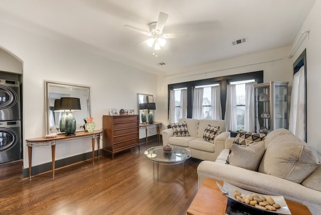 living room featuring wood finished floors, arched walkways, stacked washer / drying machine, ceiling fan, and visible vents