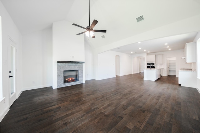 7306 Mallow Way, Venus, TX 76084 - unfurnished living room featuring ceiling fan, high vaulted ceiling, a stone fireplace, dark wood-style floors, and arched walkways