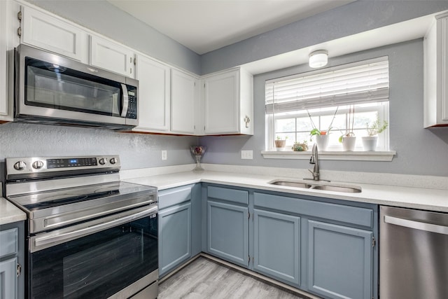 kitchen with appliances with stainless steel finishes, blue cabinetry, light countertops, and a sink