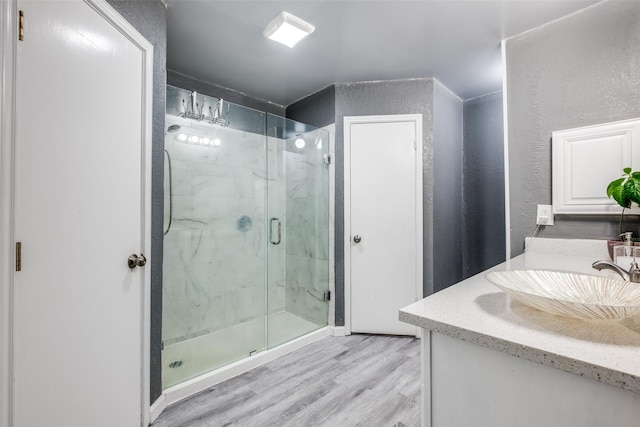 full bath featuring vanity, a marble finish shower, a textured wall, and wood finished floors