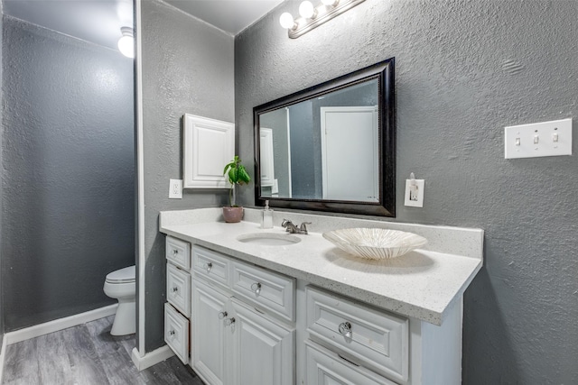 bathroom with toilet, wood finished floors, vanity, and a textured wall