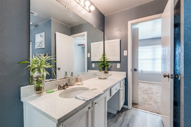 bathroom featuring wood finished floors, a textured wall, vanity, baseboards, and visible vents