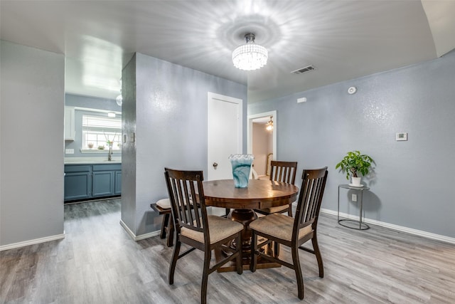 dining room with light wood finished floors, an inviting chandelier, visible vents, and baseboards