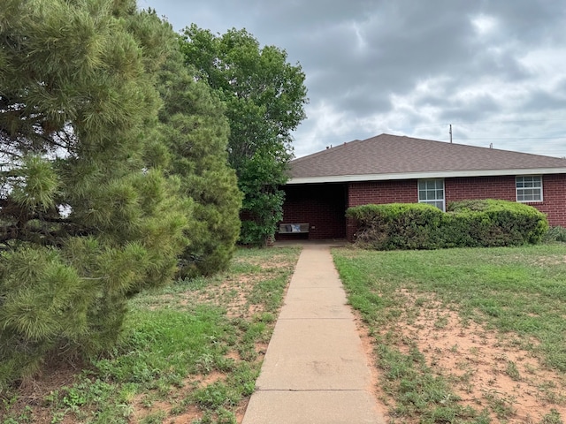 view of front of property featuring roof with shingles, a front yard, and brick siding