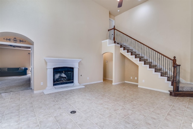 942 Lexington Dr, Rockwall, TX 75087 - unfurnished living room featuring arched walkways, a fireplace with raised hearth, stairway, a high ceiling, and light tile patterned flooring