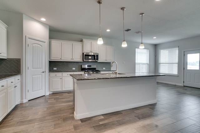 kitchen with dark stone counters, stainless steel appliances, backsplash, a sink, and light wood-type flooring