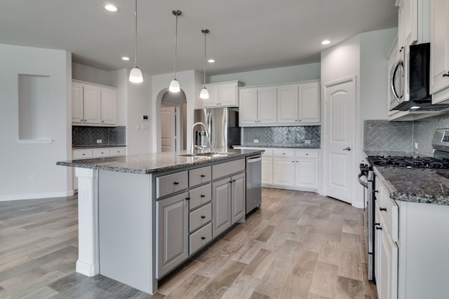 kitchen featuring light wood-style flooring, arched walkways, appliances with stainless steel finishes, and decorative backsplash