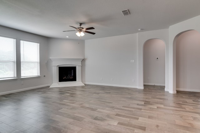 unfurnished living room featuring light wood-style floors, visible vents, a ceiling fan, and arched walkways