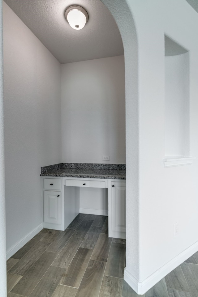 unfurnished office with arched walkways, built in study area, a textured ceiling, and dark wood-type flooring