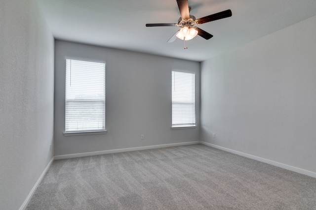 carpeted spare room featuring baseboards and a ceiling fan