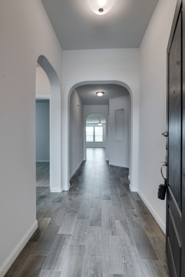 hallway featuring arched walkways, wood finished floors, and baseboards