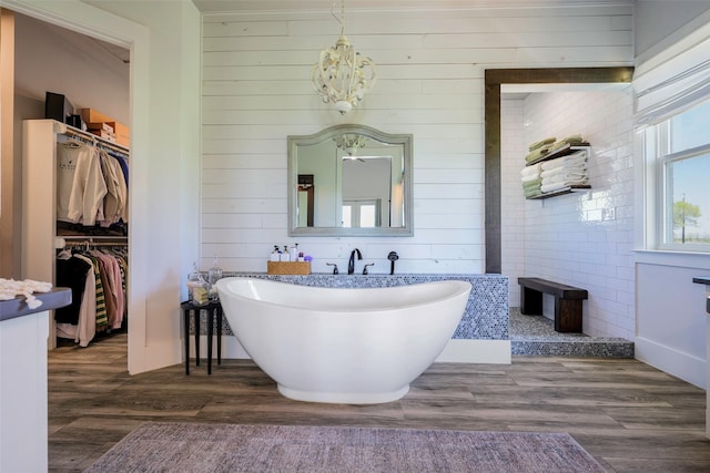 full bathroom featuring a notable chandelier, a freestanding tub, wood finished floors, and a spacious closet