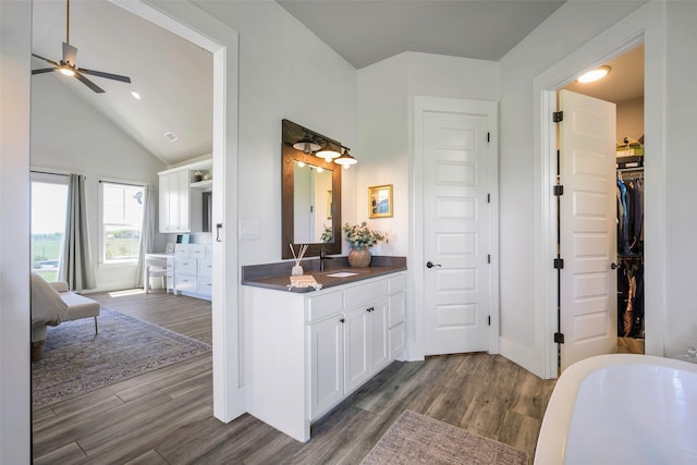ensuite bathroom with baseboards, wood finished floors, ceiling fan, vanity, and a soaking tub