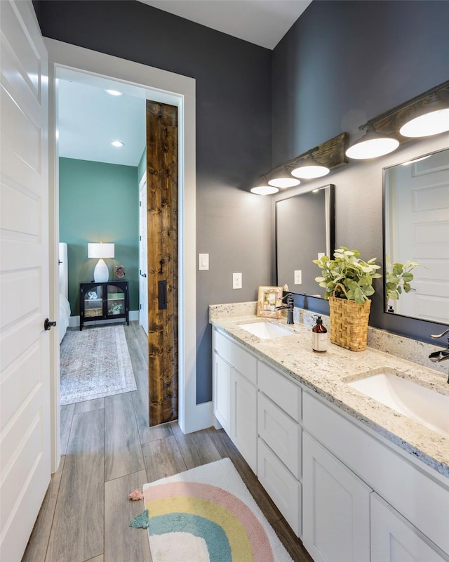 ensuite bathroom with double vanity, wood finished floors, connected bathroom, and a sink