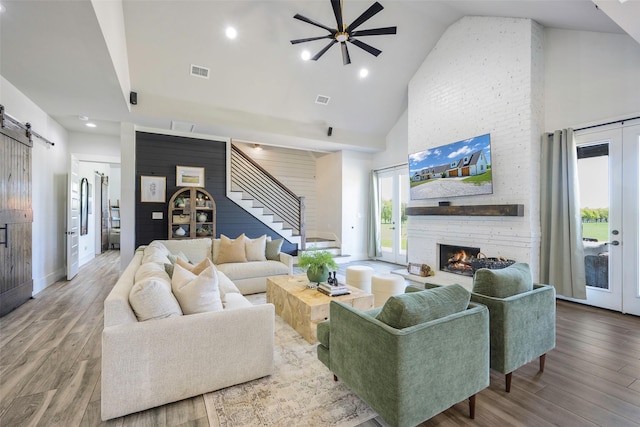 living room featuring visible vents, a barn door, ceiling fan, high vaulted ceiling, and stairs