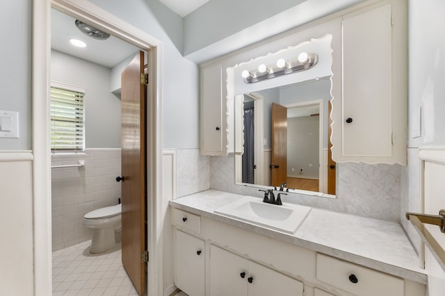 bathroom featuring a wainscoted wall, toilet, tile walls, vanity, and tile patterned flooring