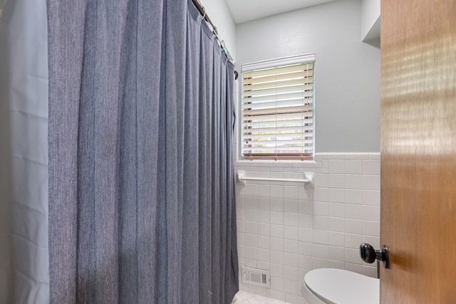 full bathroom featuring tile walls, tile patterned floors, toilet, a wainscoted wall, and visible vents