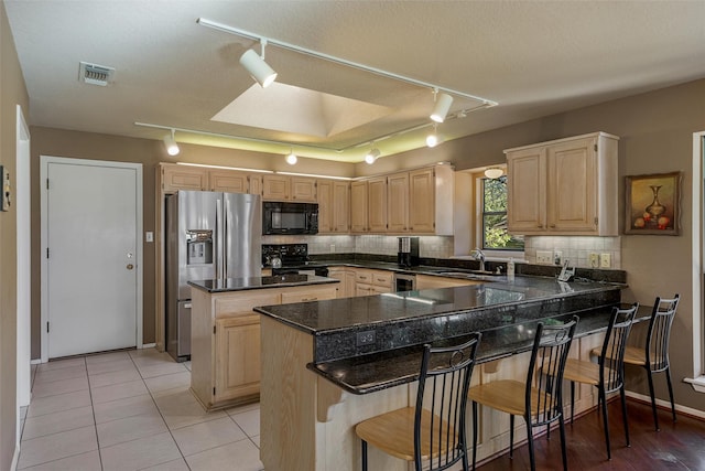 kitchen with a sink, black microwave, light brown cabinetry, rail lighting, and stainless steel refrigerator with ice dispenser