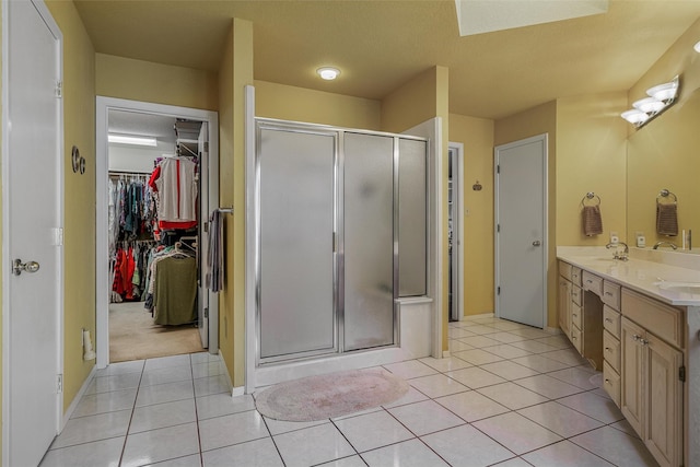 full bathroom featuring tile patterned flooring, a shower stall, double vanity, a sink, and a walk in closet