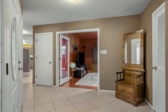 hall featuring a textured ceiling, light tile patterned floors, and baseboards