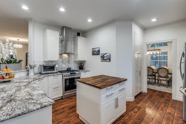 kitchen with butcher block countertops, an inviting chandelier, appliances with stainless steel finishes, and wall chimney range hood