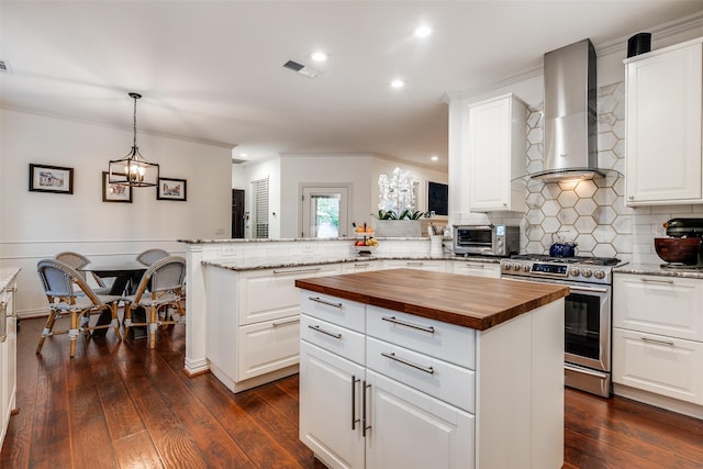kitchen with wall chimney range hood, visible vents, stainless steel gas stove, butcher block countertops, and a peninsula