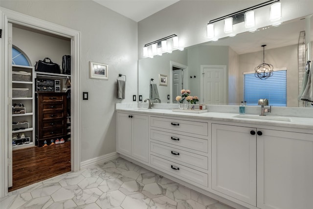 bathroom featuring a sink, marble finish floor, double vanity, baseboards, and a spacious closet