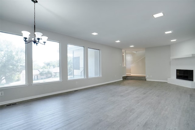 unfurnished living room featuring an inviting chandelier, a glass covered fireplace, visible vents, baseboards, and wood finished floors