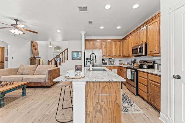 kitchen featuring light wood finished floors, stainless steel appliances, a kitchen bar, a ceiling fan, and ornamental molding
