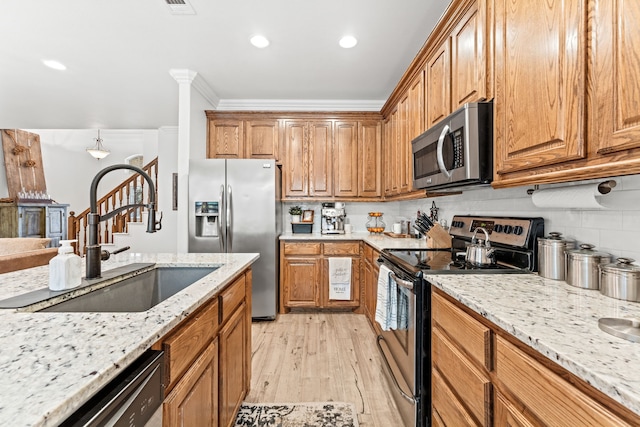kitchen with a sink, stainless steel appliances, light wood-style floors, decorative backsplash, and light stone counters