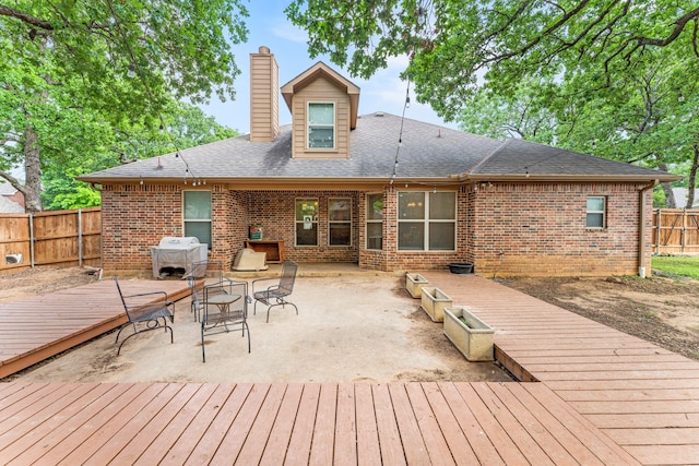rear view of house with a chimney, brick siding, a wooden deck, and a fenced backyard