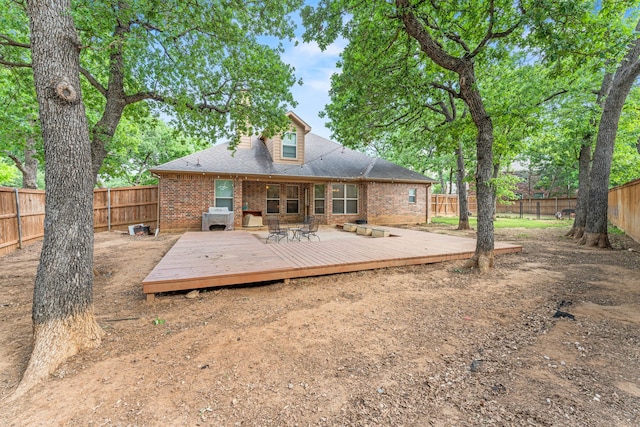 rear view of property featuring a deck, roof with shingles, a fenced backyard, and brick siding