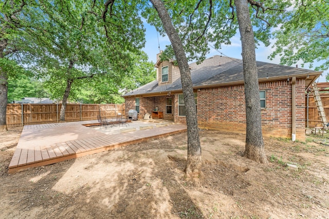 back of property featuring a wooden deck, a shingled roof, brick siding, and a fenced backyard