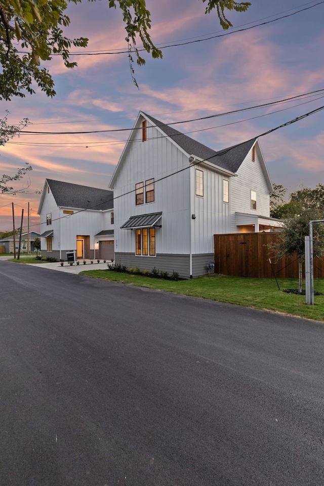 modern farmhouse featuring a standing seam roof, a shingled roof, board and batten siding, aphalt driveway, and fence