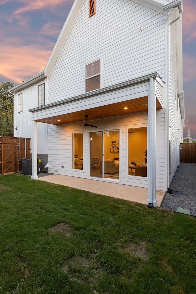 back of house at dusk with a lawn, fence, central AC unit, and a patio area