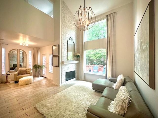 living room with a notable chandelier, a stone fireplace, light wood finished floors, and a towering ceiling