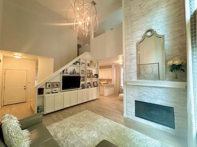 living area featuring stairway, a chandelier, a fireplace, a towering ceiling, and wood finished floors