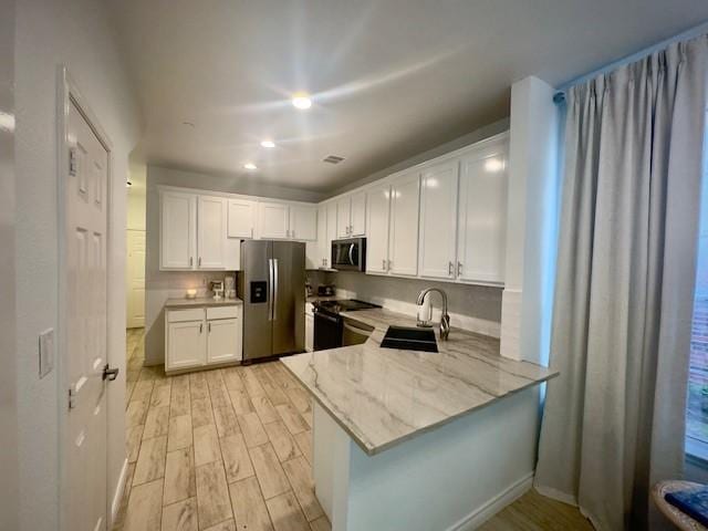 kitchen featuring light stone counters, white cabinets, a sink, stainless steel appliances, and light wood finished floors
