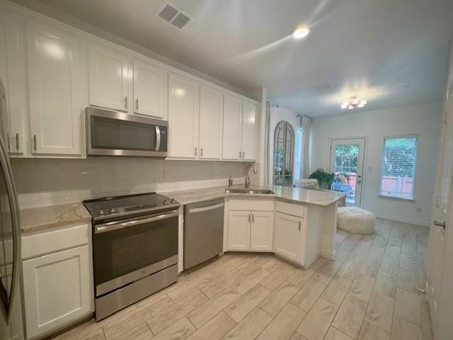 kitchen with appliances with stainless steel finishes, light countertops, white cabinets, a sink, and a peninsula
