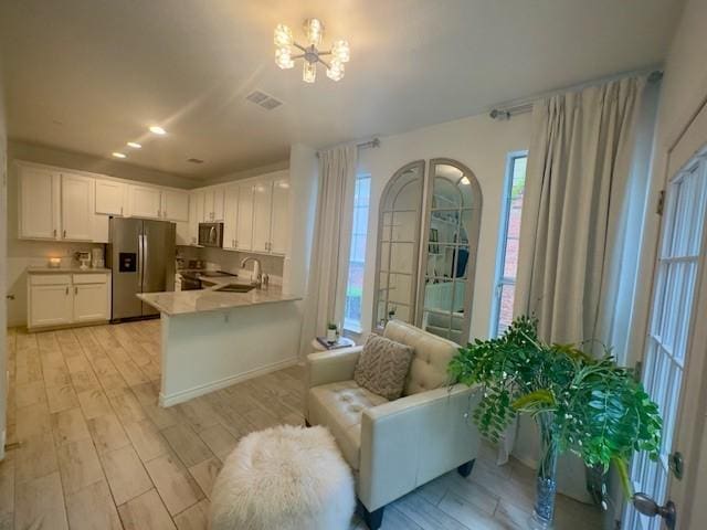 kitchen with light wood-type flooring, a notable chandelier, stainless steel fridge with ice dispenser, and light countertops