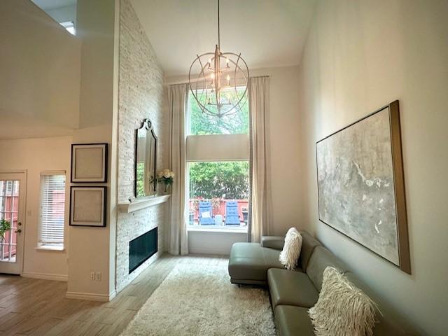 living area with a notable chandelier, a stone fireplace, wood finished floors, and baseboards