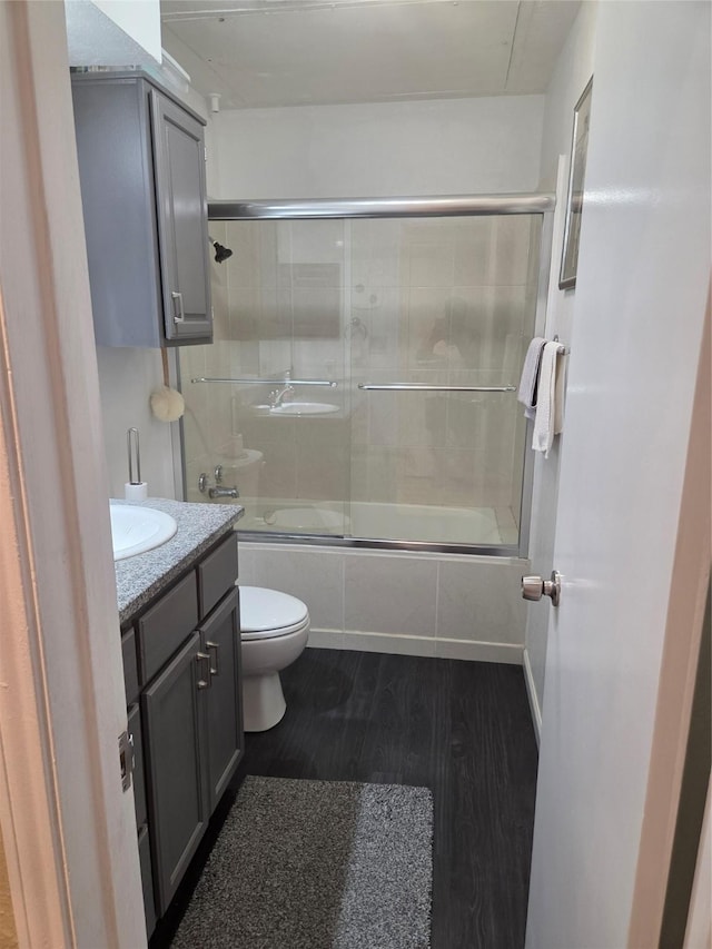 full bath with combined bath / shower with glass door, wood finished floors, toilet, and vanity
